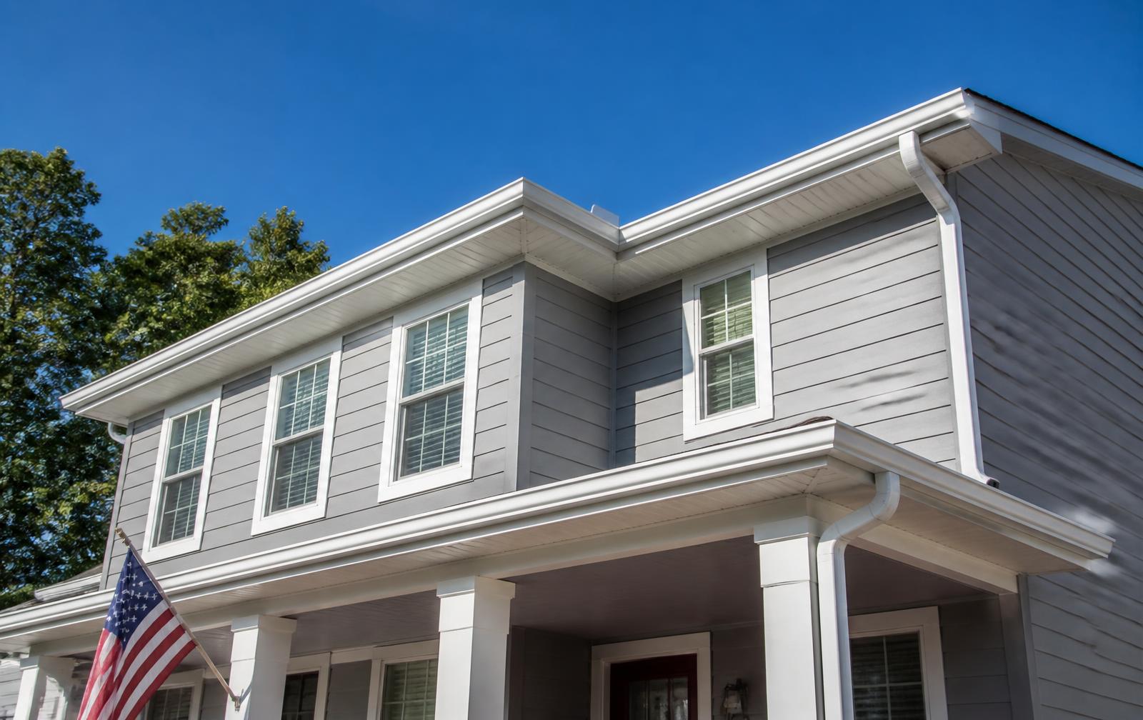 Newly installed white seamless gutters along the roofline of a gray suburban home